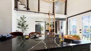 Een moderne keuken met een marmeren aanrechtblad, een houten ladder en uitzicht op de stad door grote ramen.