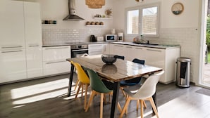 A modern kitchen with white cabinets, a dining table with chairs, a stove, a microwave, and a sink. - Chic and warm!  Modern house near the beach Baie de Morgat (Crozon)