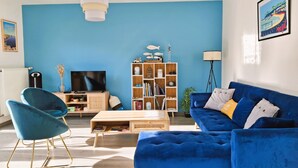 A living room with a blue sofa, a blue chair, a wooden coffee table, a TV, a bookshelf, and a floor lamp. - Chic and warm!  Modern house near the beach Baie de Morgat (Crozon)
