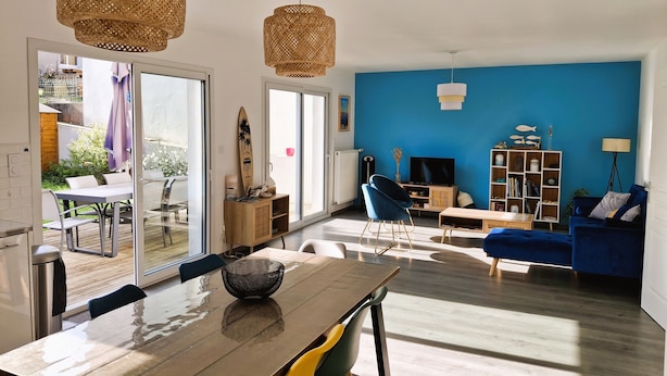 A modern living room with a blue accent wall, a dining area with a wooden table, and a blue sofa. - Chic and warm!  Modern house near the beach Baie de Morgat (Crozon)