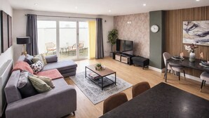 Una sala de estar moderna con sofá, mesa de centro, televisor, comedor y puerta de vidrio corrediza que da a un espacio exterior.