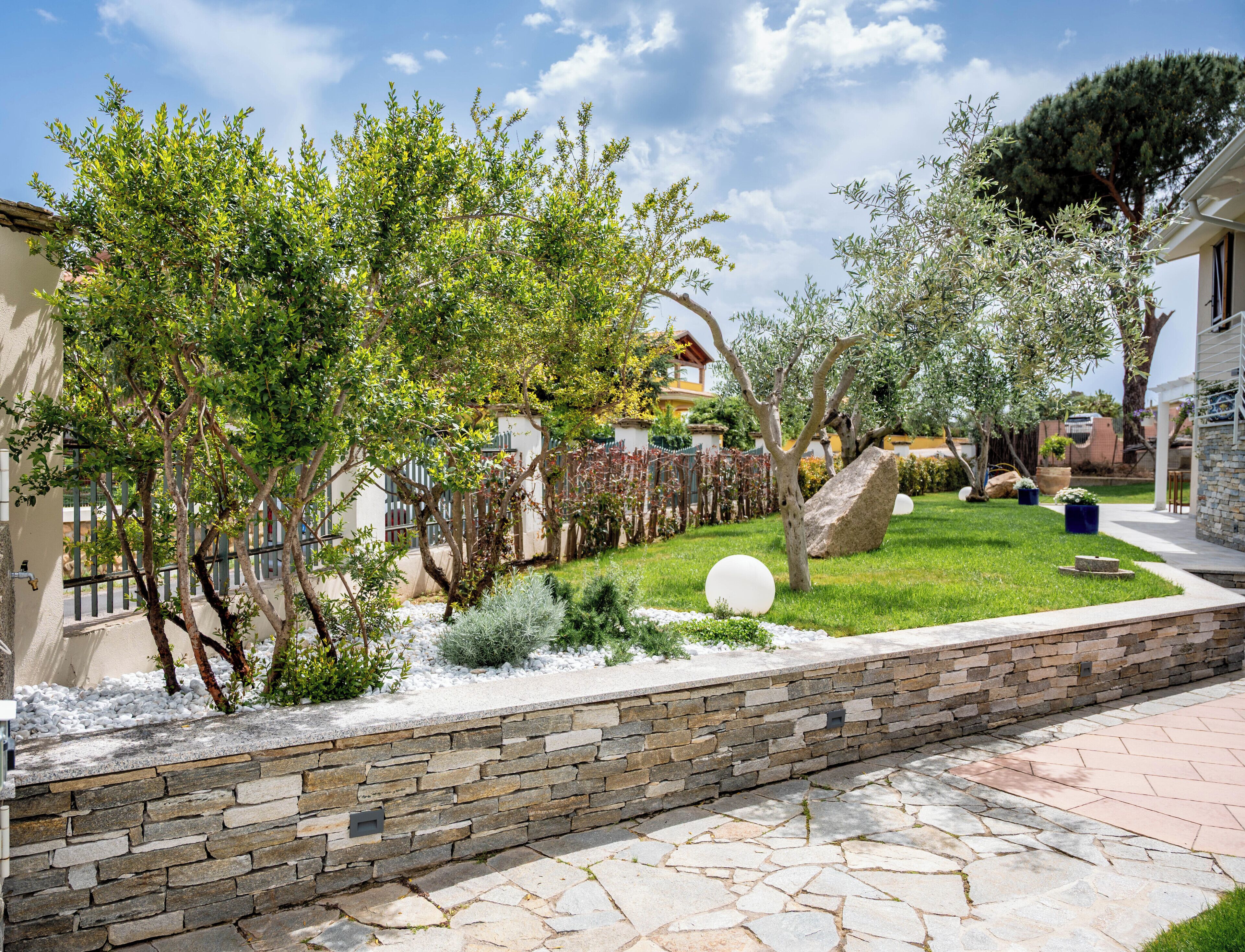 Un jardin aménagé avec un mur en pierre, une variété d’arbres et un chemin pavé.