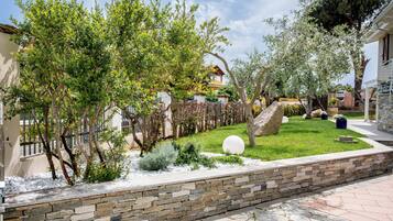 A landscaped garden with a stone wall, a variety of trees, and a paved walkway.