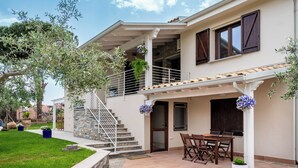 Ein zweistöckiges Haus mit überdachter Terrasse, Außenbestuhlung und einer Steintreppe.
