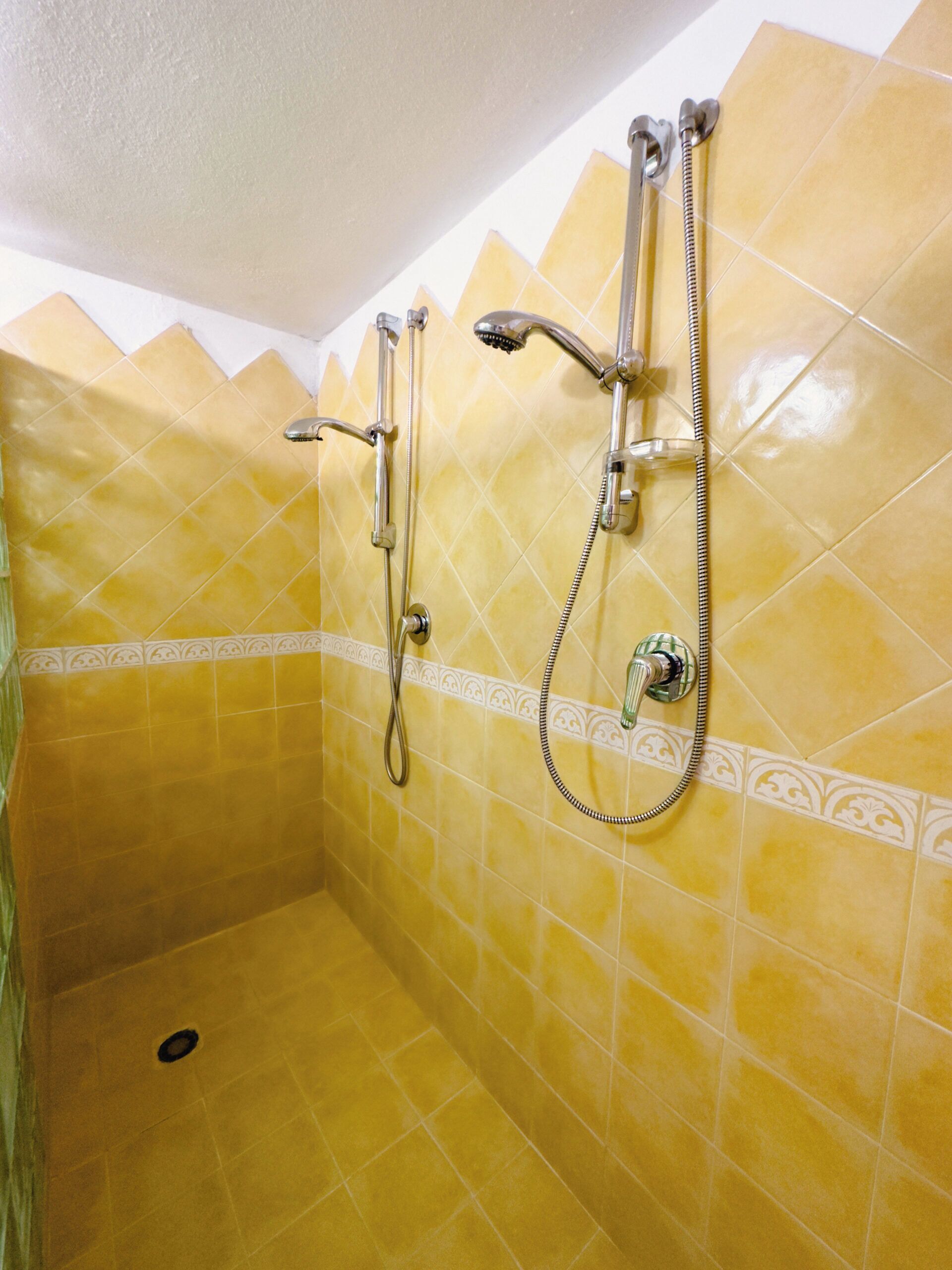 Un espacio de ducha pequeño, con azulejos amarillos, dos cabezales de ducha y un rociador manual.
