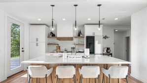 Una cocina moderna con una isla grande, armarios blancos y taburetes de bar.