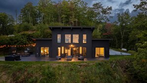 Una casa moderna de dos pisos con un patio, mobiliario exterior y vistas al bosque circundante.