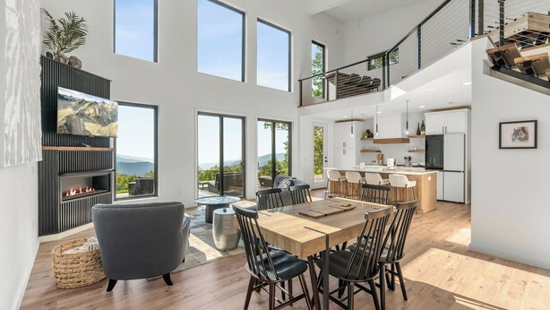 Un espacio habitable amplio con una mesa de comedor de madera, asientos cómodos, una chimenea y ventanas grandes que ofrecen vistas al exterior.