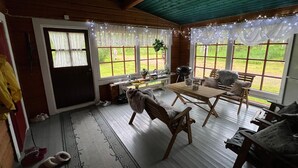 Une pièce chaleureuse avec un plafond en bois, une table, des chaises et un banc. Il y a des fenêtres avec des rideaux et une vue sur l’extérieur.