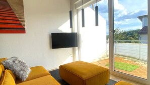 Un salon moderne comprenant un ensemble de canapés, un téléviseur à écran plat fixé au mur et une porte-fenêtre coulissante donnant sur un balcon.
