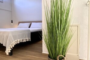 A bedroom with a bed, a bedside table, and a potted plant.