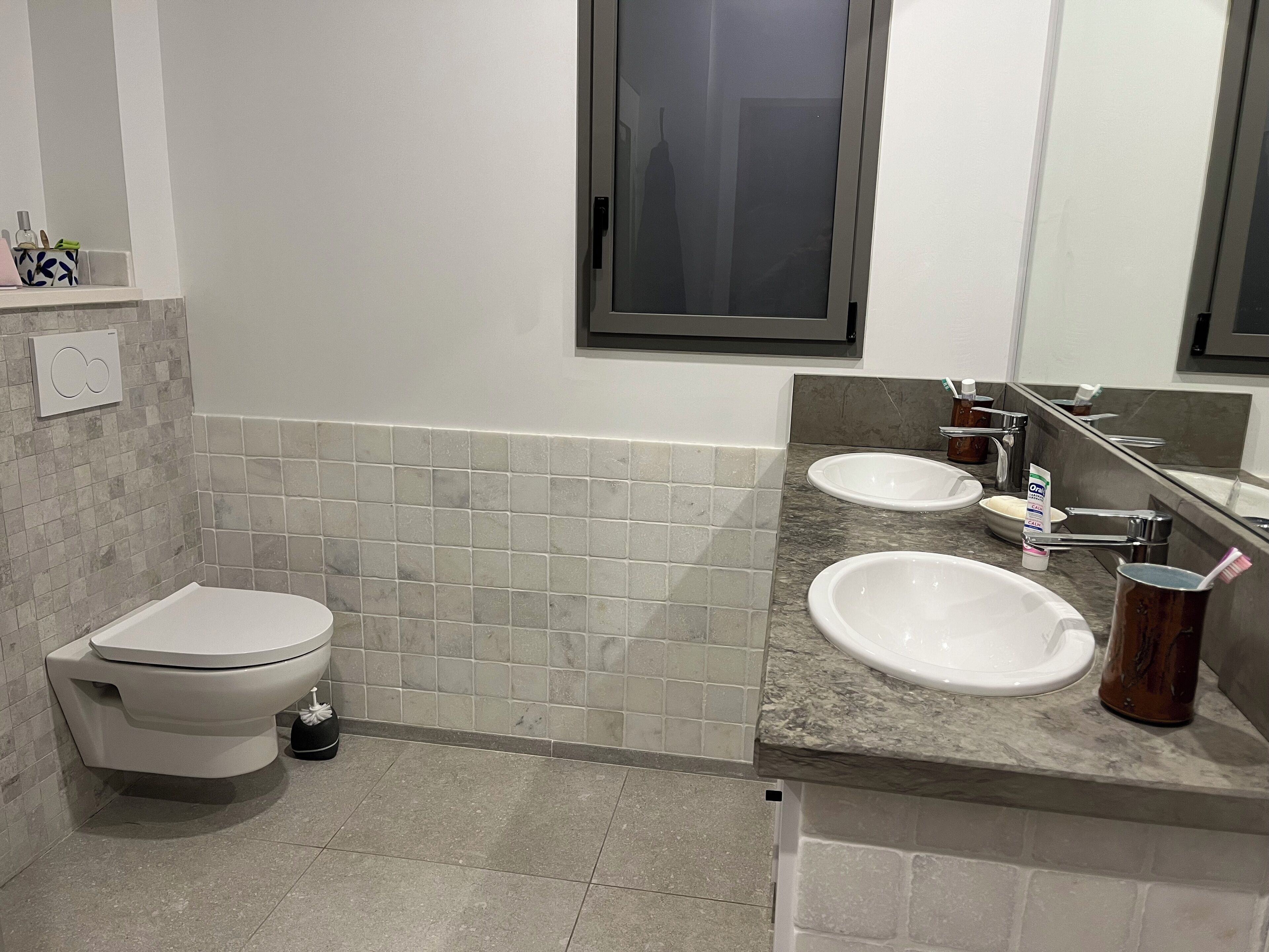 Et moderne badeværelse med toilet, to håndvaske, et spejl og et vindue.