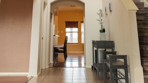 Un pasillo amplio con una escalera, un comedor con sillas y una mesa, y una vista a otra habitación.