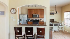 Una cocina con armarios de madera, microondas, refrigerador, cafetera y comedor con sillas y una mesa.