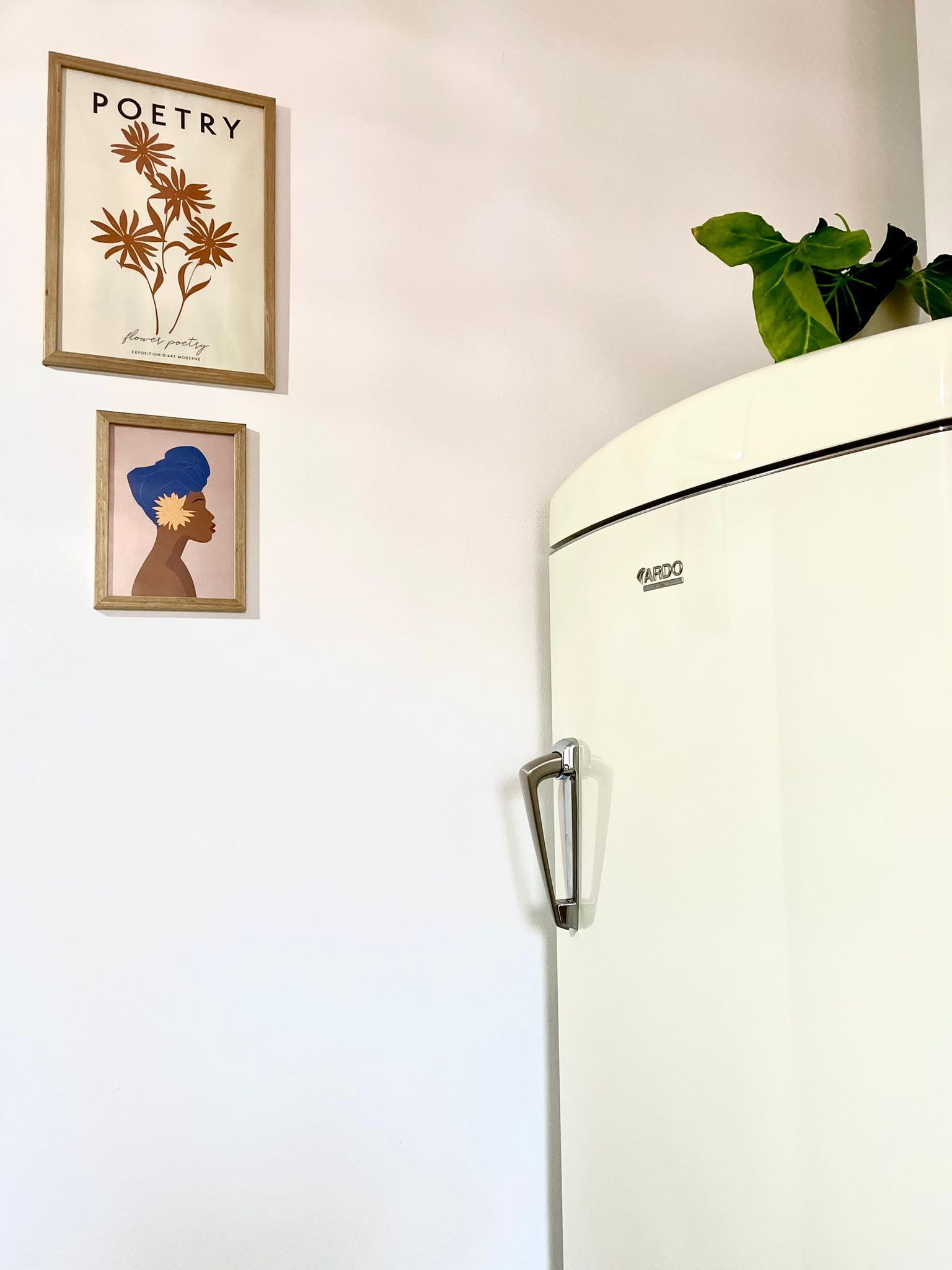 Un frigorífic blanc amb un mànec, una obra d'art amb flors i la paraula "POETRY" penjada a la paret, i un retrat emmarcat.