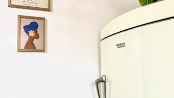 Un refrigerador blanco con manija, una obra de arte enmarcada con flores y la palabra "POETRY" en la pared, y un retrato enmarcado.