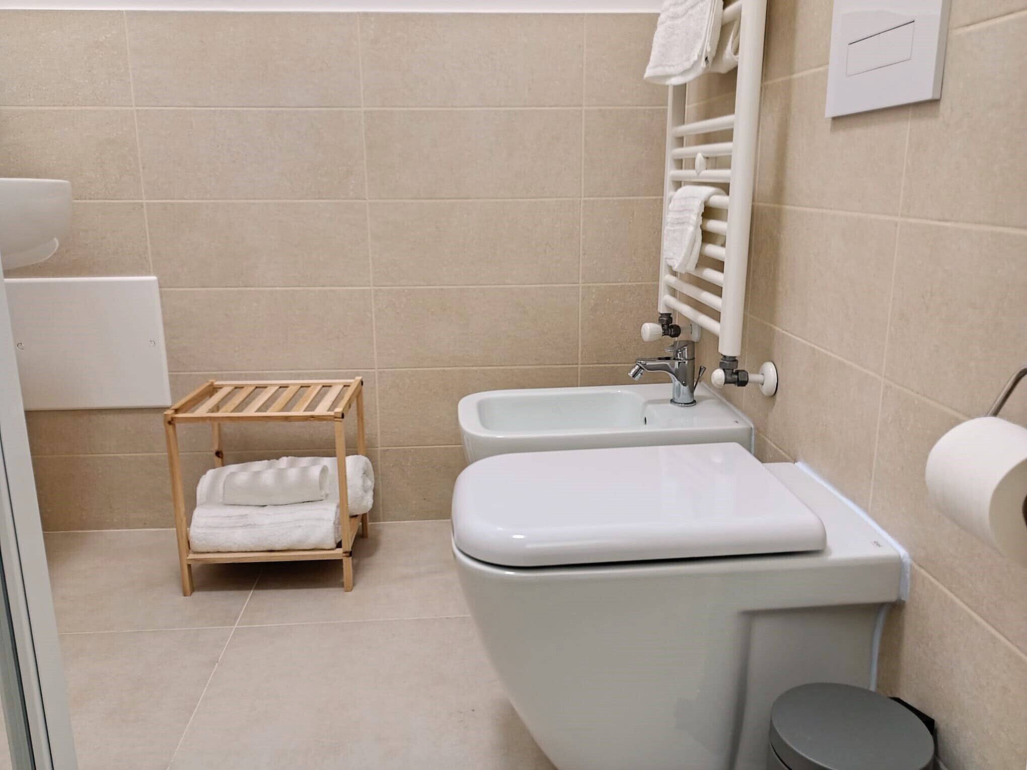 A bathroom with a toilet, bidet, and a wooden towel rack.