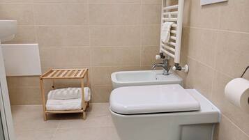 A bathroom with a toilet, bidet, and a wooden towel rack.