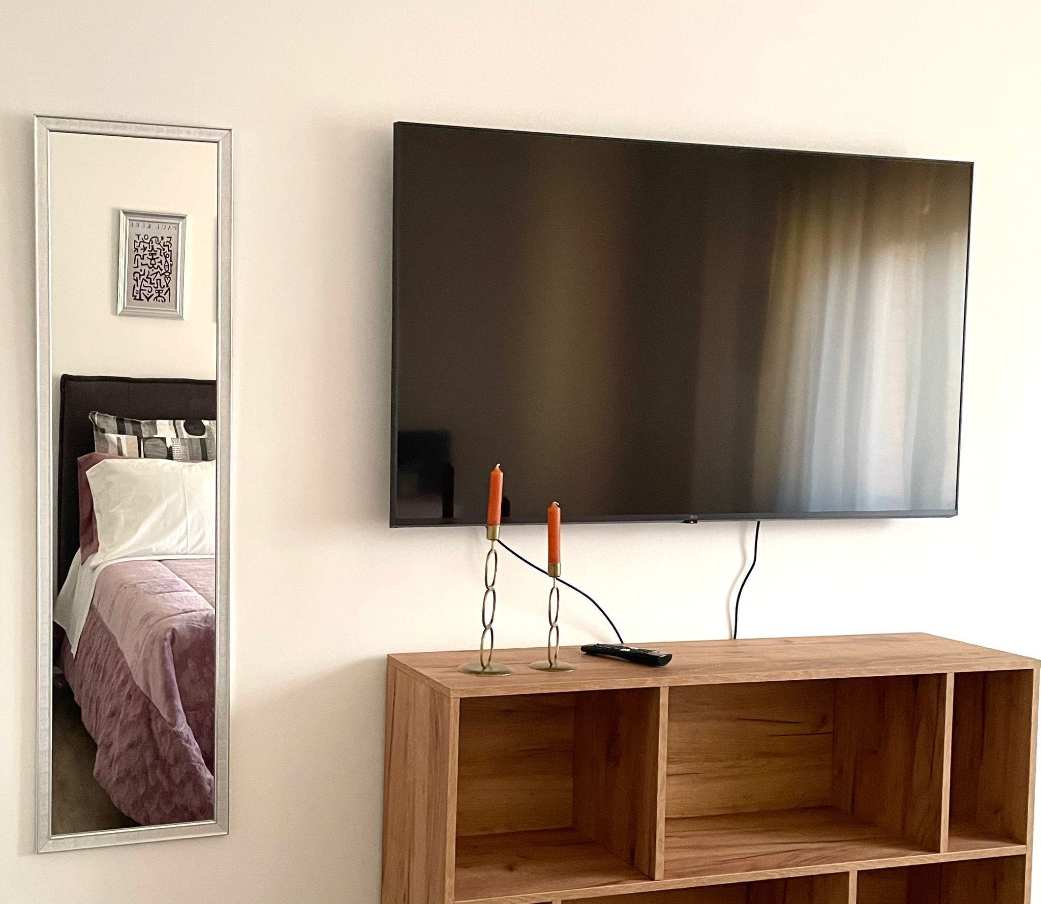 Ein Schlafzimmer mit einem Bett, einem Nachttisch mit Fernbedienung und einem an der Wand befestigten Fernseher.