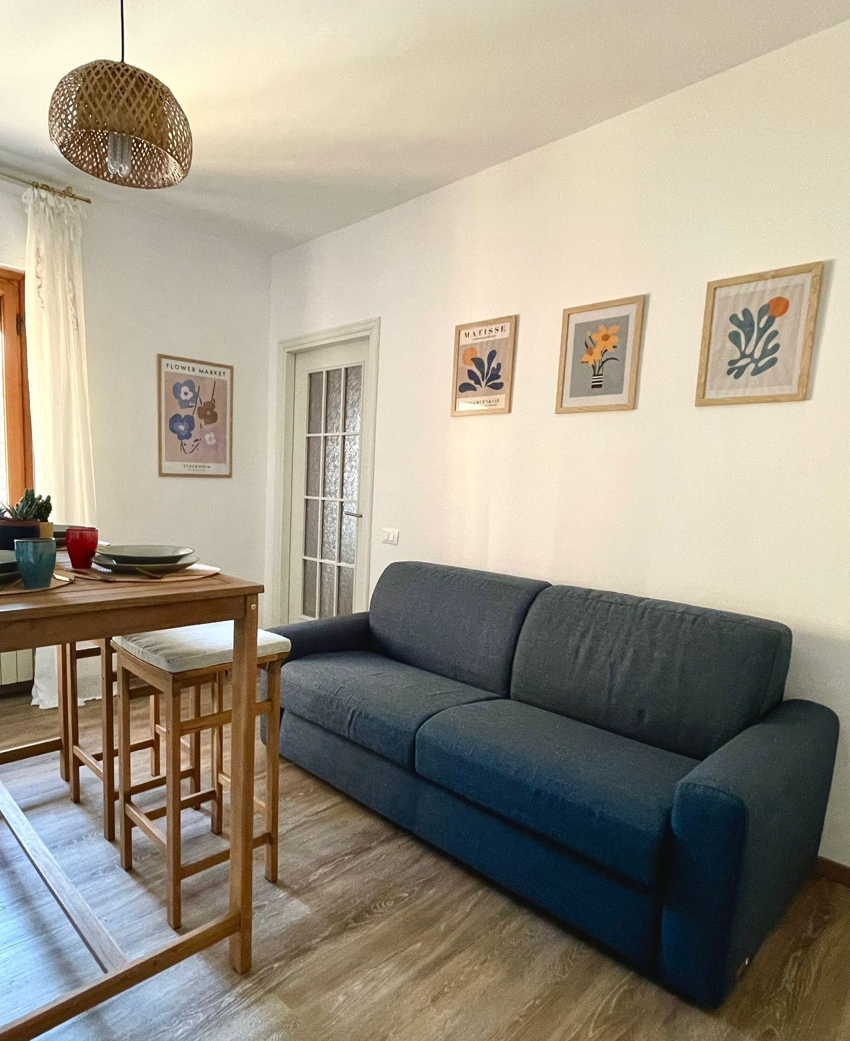 Ein Wohnzimmer mit dunkelblauem Sofa, einem Holzesstisch mit zwei Stühlen und einer Hängeleuchte.