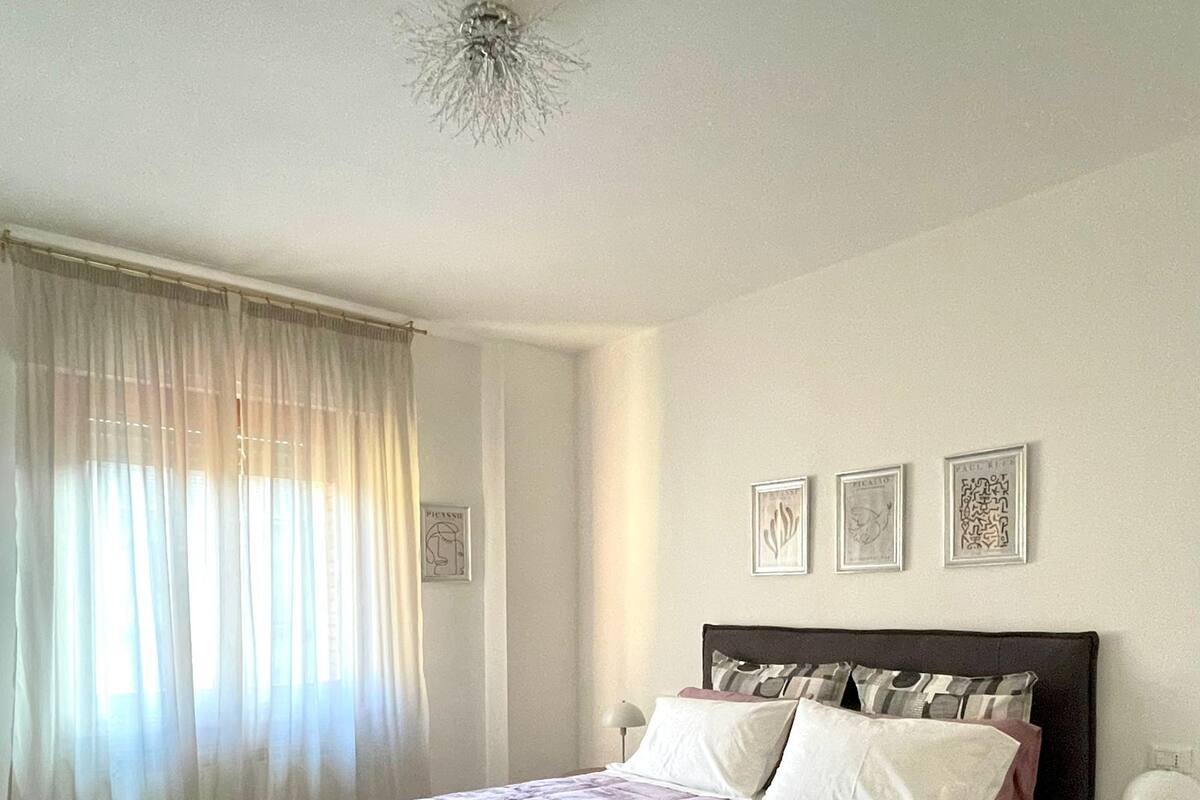 A bedroom with a large bed, a bedside table, a lamp, and a window with curtains.