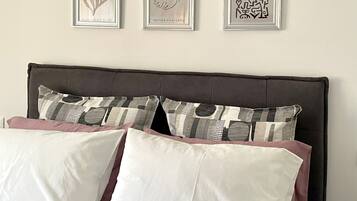 Ein Bett mit weißer und rosa Bettwäsche, ein dunkles Kopfteil und drei gerahmte Kunstwerke an der Wand.