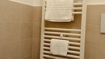 Un baño con un lavamanos blanco, un perchero con tres toallas blancas y paredes de cerámica en tonos beige.