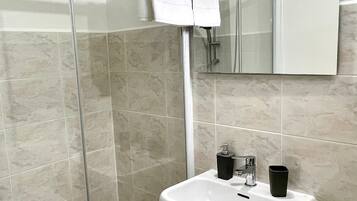 Une salle de bain avec une douche à parois de verre, un lavabo blanc et un miroir au-dessus du lavabo.