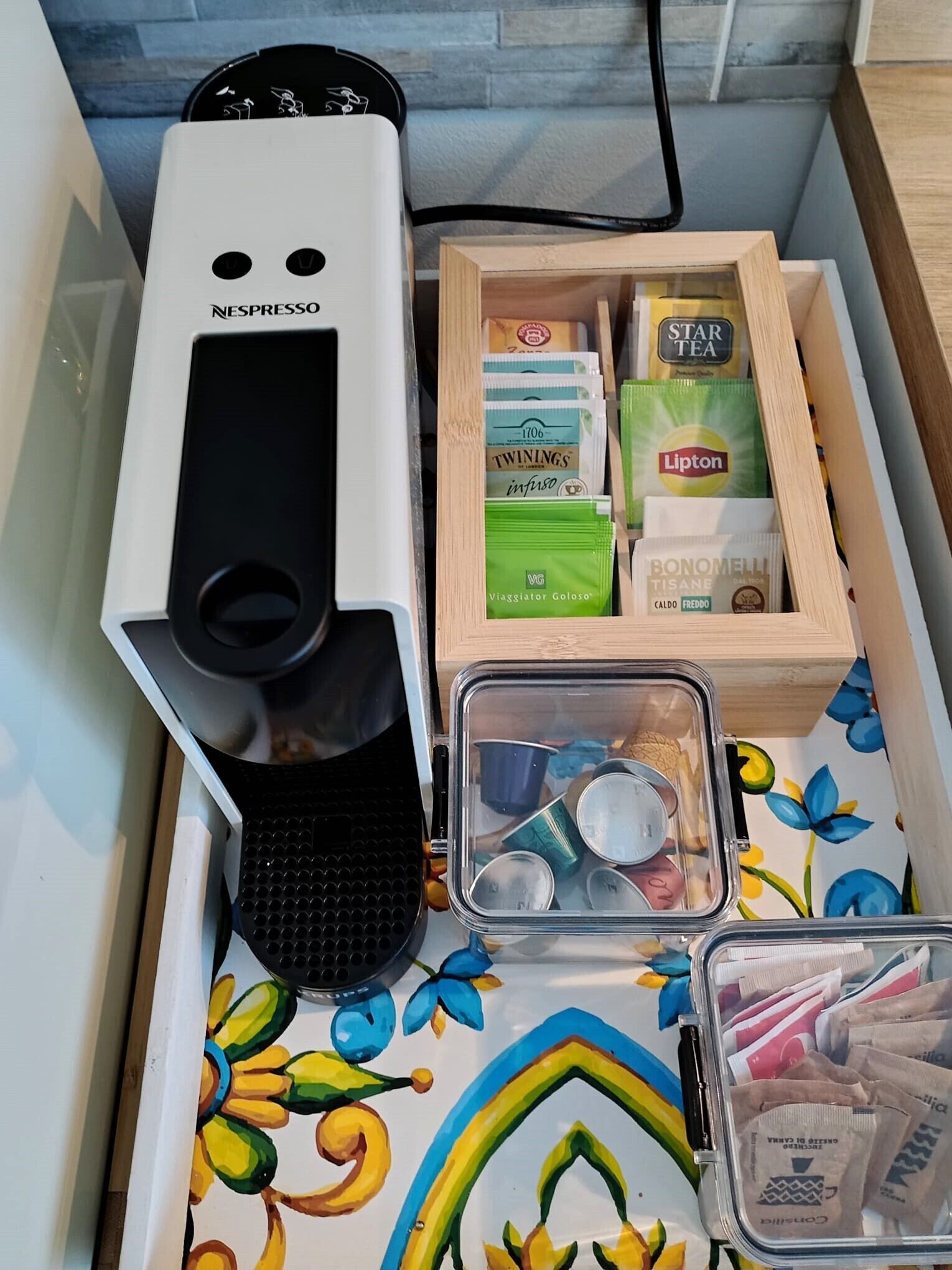 A Nespresso coffee machine, a wooden box with coffee pods, a Lipton tea box, and a container with coffee cups and filters.