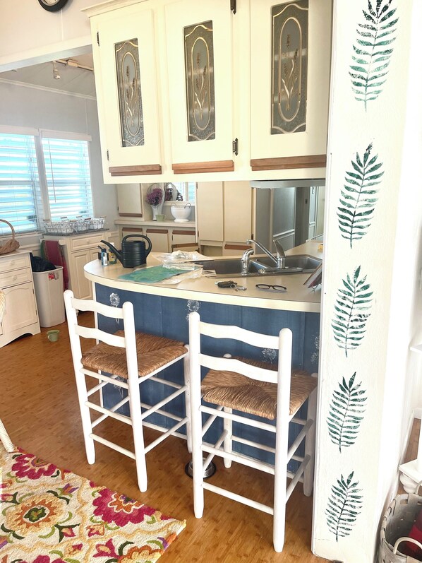 A kitchen with white cabinets, a blue island, and two wicker chairs.