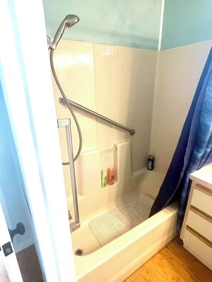 A shower with a handheld showerhead, a handheld shower control, and a small shelf with toiletries.