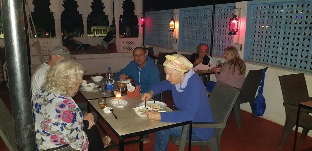 A group of people dining at an outdoor restaurant with a view of the cityscape.