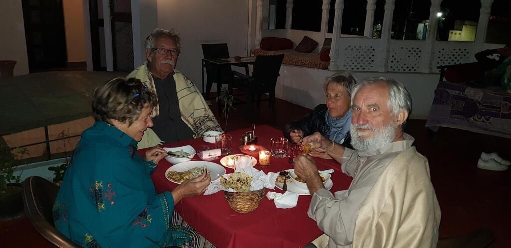 Un grupo de personas cenando en una mesa con mantel rojo, rodeadas de sillas y una ventana con vistas.