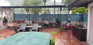Ein Straßencafé mit Tischen, Stühlen und einer kleinen Theke, sowie einem Bereich mit einer grünen Plane.