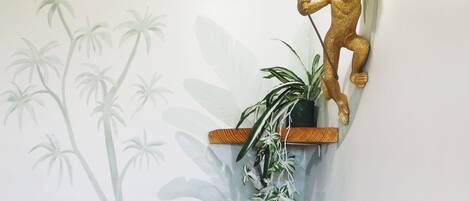 A wall-mounted golden monkey sculpture holding a light fixture, a potted plant, and a wall with a tropical plant mural.