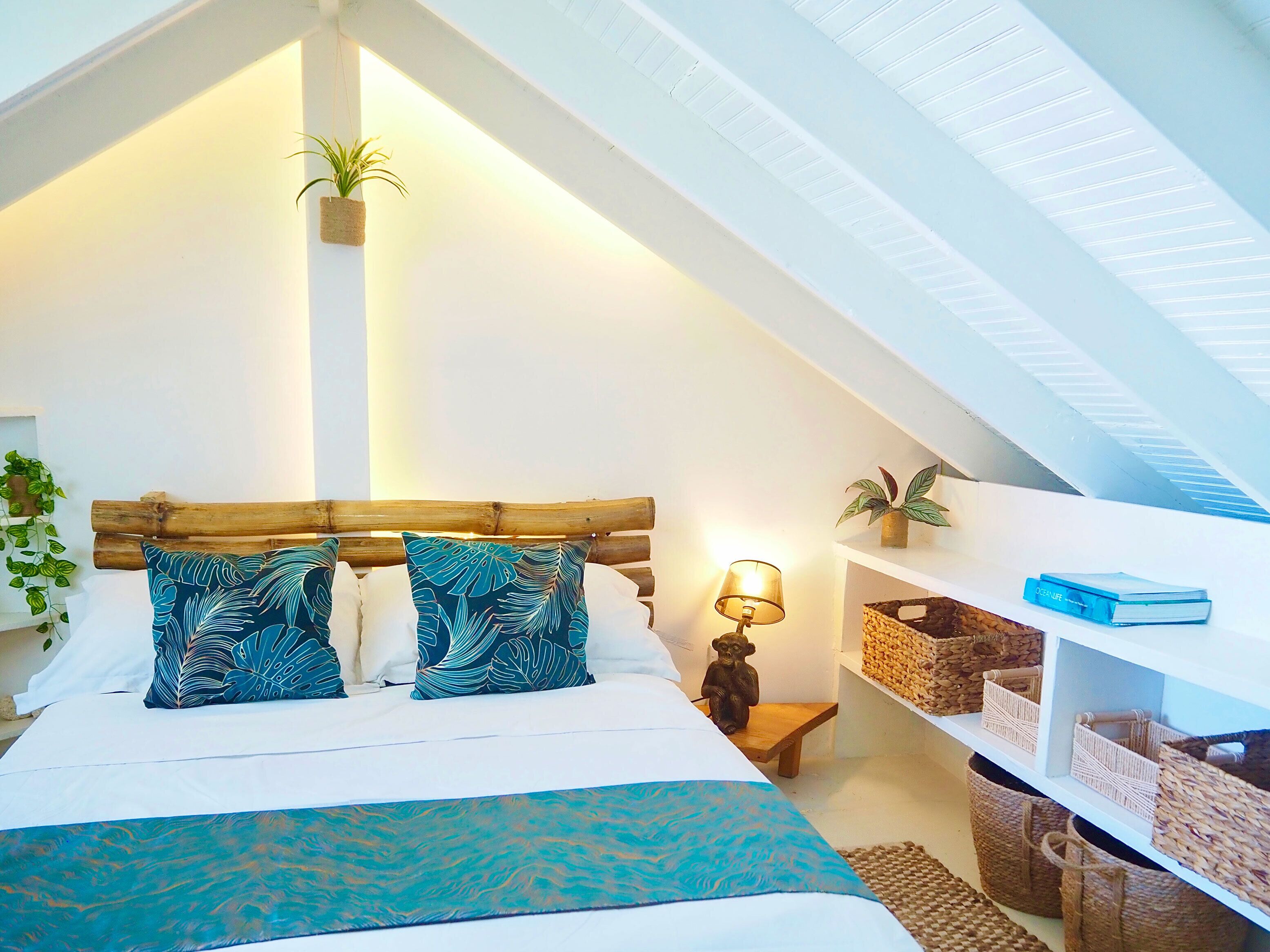 A cozy bedroom with a sloped ceiling, a bed with patterned pillows, a bedside lamp, and shelves with baskets.