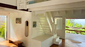Ein modernes Interieur mit einer Treppe zu einem Balkon, Holzboden und Blick auf Grün.