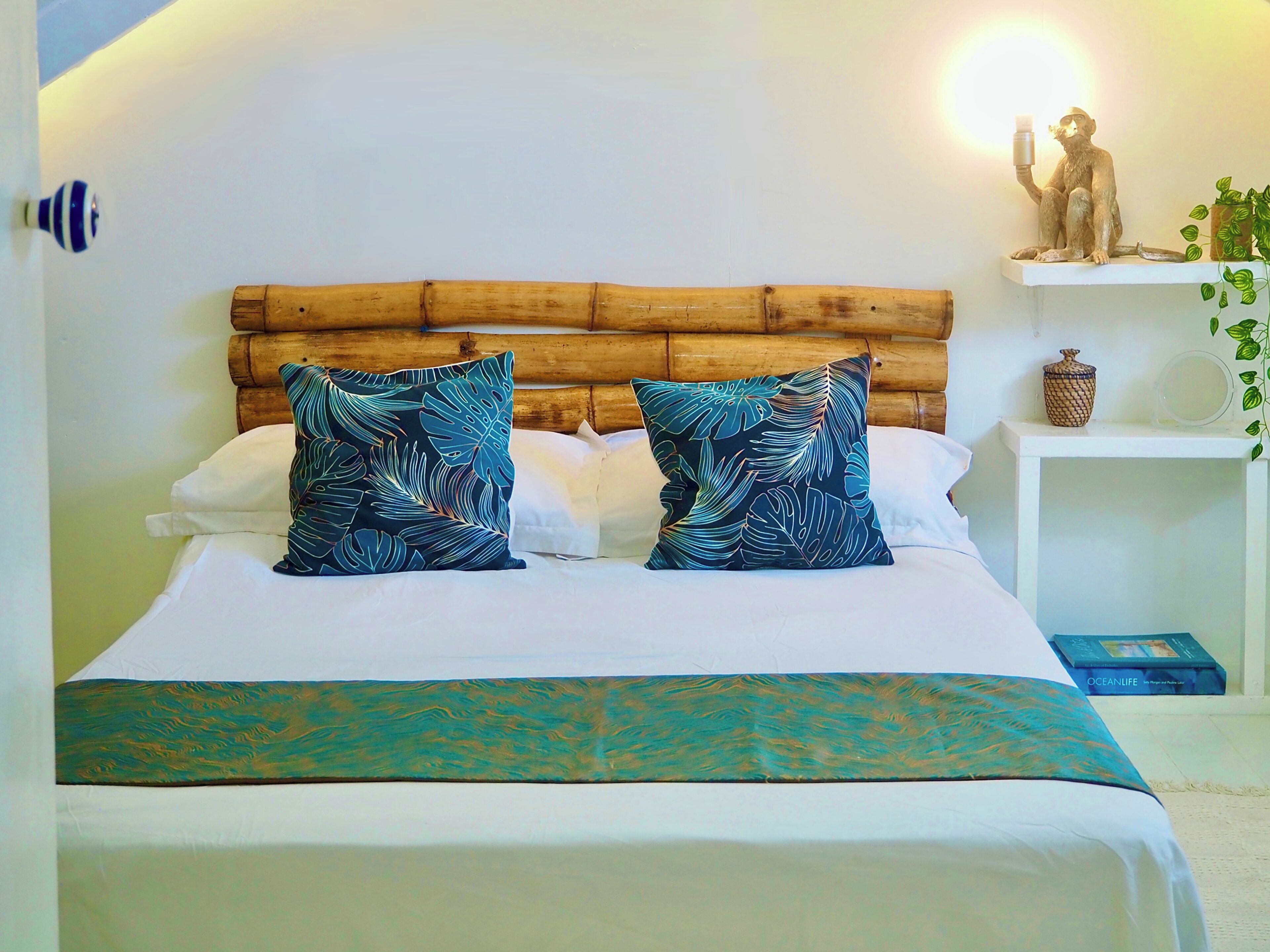 Un lit avec une tête de lit en bois, deux coussins à motifs, un couvre-lit blanc et une couverture turquoise.