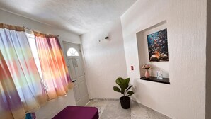 A room with a bed, a potted plant, a painting on the wall, and a window with curtains.