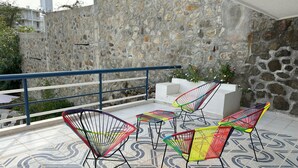 A rooftop patio with colorful chairs and a patterned floor, a stone wall, and a railing.