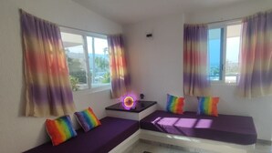 A room with two purple sofas, a small table with a neon light, and windows with colorful curtains.