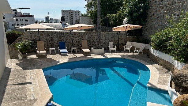 A swimming pool with lounge chairs and umbrellas, surrounded by stone walls and greenery.