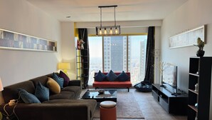 Una sala de estar moderna con un sofá, una mesa de centro y un televisor. Hay un ventanal con vistas a la ciudad.