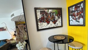 Una sala de estar moderna con una pared de acento amarilla, una mesa redonda negra con taburetes y dos obras de arte enmarcadas.