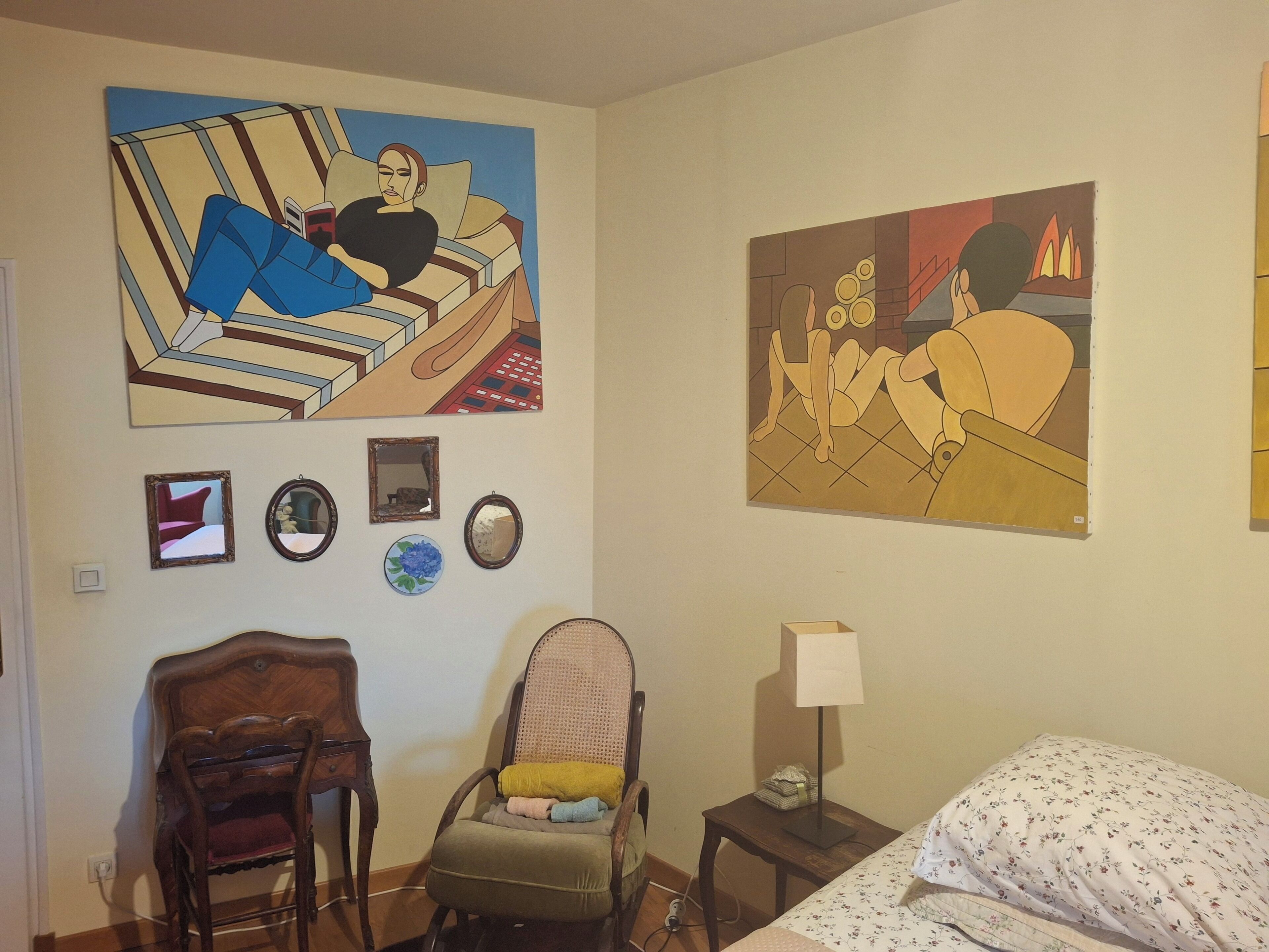 Ein Schlafzimmer mit einem Bett, einem Sessel, einem Nachttisch mit Lampe und zwei Bildern an der Wand.