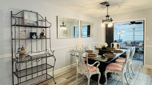 Un coin repas comprenant un présentoir métallique où sont exposés des objets décoratifs, une table à manger avec des chaises, et une vue sur le salon.