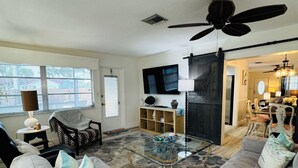 Un salon avec un grand canapé, une table basse en verre, un téléviseur et un ventilateur de plafond.