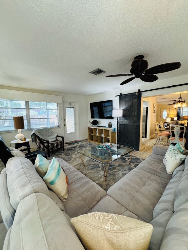 A living room with a large sofa, a glass coffee table, a TV, and a ceiling fan.