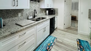 Une cuisine moderne avec des meubles blancs, des comptoirs en granit et un lave-vaisselle noir. Un tapis bleu à motifs marins recouvre le sol.