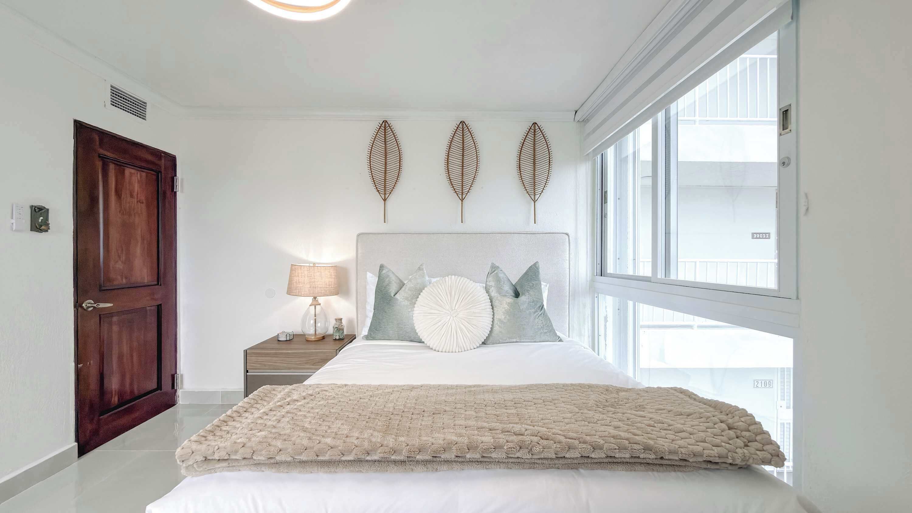 A bedroom with a bed, a nightstand, a lamp, a door, and a window.